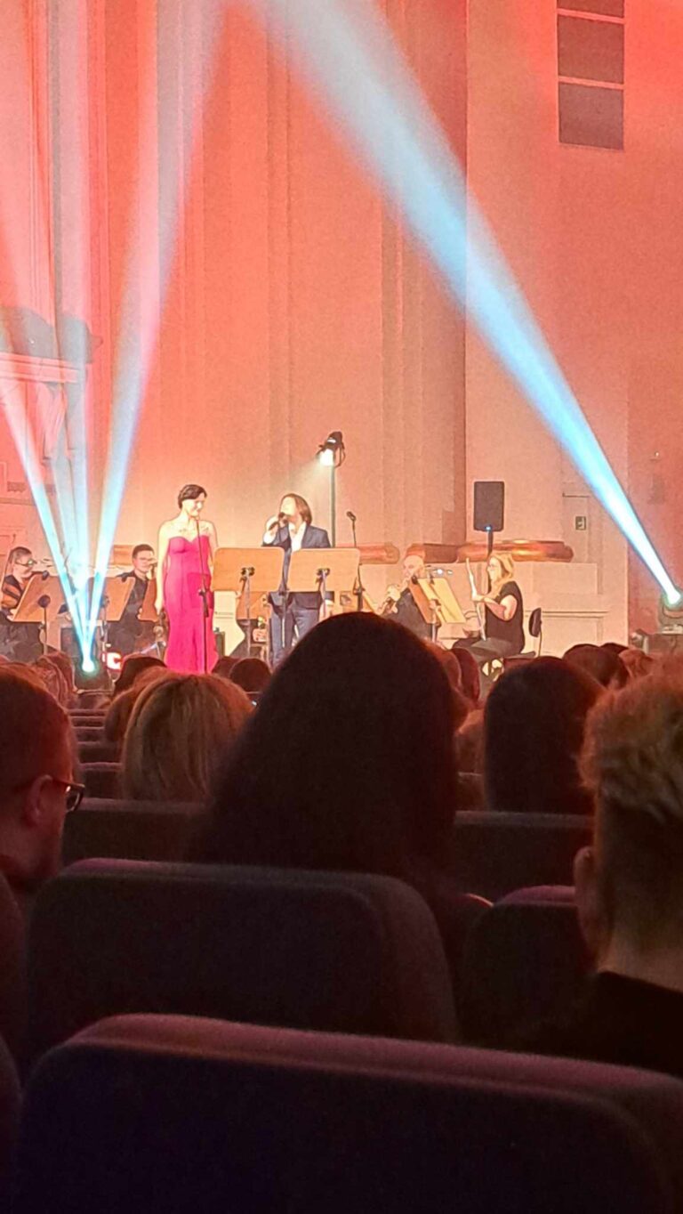 Na scenie stoi kobieta w czerwonej sukience