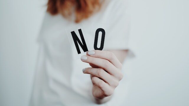 Dłoń kobiety, która trzyma dwie litery składające się na wyraz NO, który określa asertywną postawę